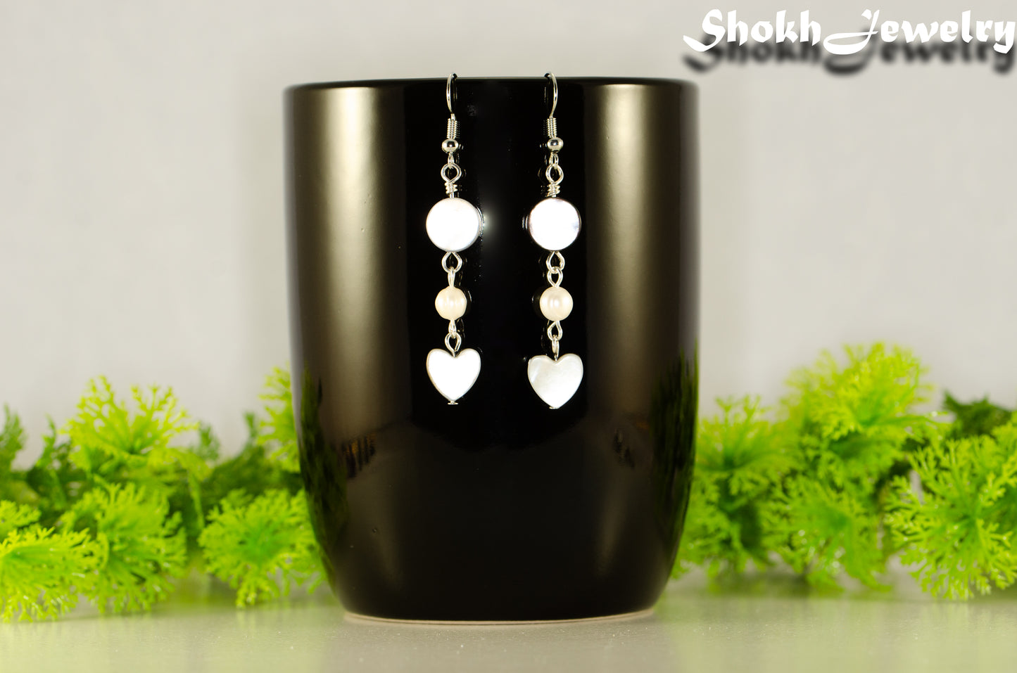 Grey Seashell and White Pearl Earrings displayed on a coffee mug.